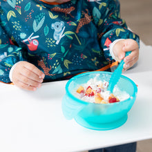 Load image into Gallery viewer, Close-up of a child in a colorful bib eating fruit and yogurt from a Bumkins Silicone First Feeding Set: Blue Jelly on a white high chair tray.