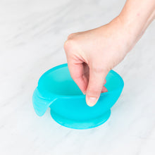 Load image into Gallery viewer, A hand holds a Bumkins Silicone First Feeding Set: Blue Jelly, demonstrating the suction cup bottom on a marble surface.