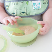 Load image into Gallery viewer, Close-up of a baby holding a Bumkins Silicone First Feeding Set: Green Jelly with applesauce, wearing a bib with animal designs.