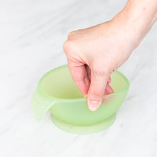 Load image into Gallery viewer, A hand holds a Bumkins Silicone First Feeding Set: Green Jelly, demonstrating the suction cup bottom on a marble surface.