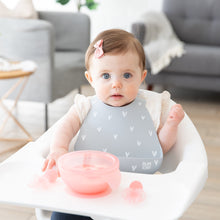 Load image into Gallery viewer, A baby in a gray bib with a bow sits in a high chair with a Bumkins Silicone First Feeding Set: Pink Jelly on the tray.