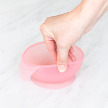 Load image into Gallery viewer, A hand holds a Bumkins Silicone First Feeding Set: Pink Jelly, demonstrating the suction cup bottom on a marble surface.