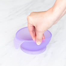 Load image into Gallery viewer, A hand holds a Bumkins Silicone First Feeding Set: Purple Jelly, demonstrating the suction cup bottom on a marble surface.