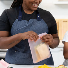 Load image into Gallery viewer, A person in blue apron places a sandwich into a Bumkins Silicone Flat Reusable Bag 2 Pack, Pink in a bright kitchen.