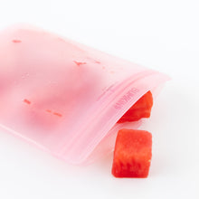 Load image into Gallery viewer, A partially open Bumkins Silicone Flat Reusable Bag 2 Pack, Pink with fresh watermelon cubes spilling out onto a white background.