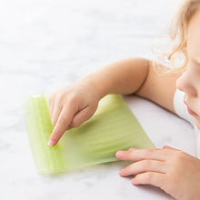 Load image into Gallery viewer, A child exploring a Bumkins Silicone Flat Reusable Bag 2 Pack, Sage on a marble countertop.