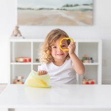 Load image into Gallery viewer, A child playfully holds a bell pepper slice over one eye at a white table with a Bumkins Silicone Flat Reusable Bag 2 Pack, Sage.