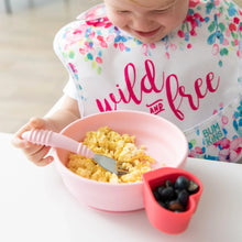 Load image into Gallery viewer, A child eats scrambled eggs from Bumkins Silicone Grip Bowl: Pink, using a pink fork, at a white table. Berries await nearby in a red cup.