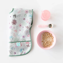 Load image into Gallery viewer, A folded floral bib, Bumkins Silicone Grip Bowl: Pink with cereal and milk, a pink cup, and pink spoon neatly placed on a white background.