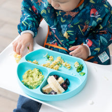Load image into Gallery viewer, A child in a colorful bib enjoys pasta, fruit, and avocado from a Bumkins Silicone Grip Dish: Blue on a high chair tray.
