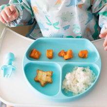 Load image into Gallery viewer, A baby in a dinosaur bib enjoys rice, sweet potato, and a star treat from a Bumkins Silicone Grip Dish: Blue with a blue fork nearby.