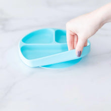 Load image into Gallery viewer, A hand holds a Bumkins Silicone Grip Dish: Blue, demonstrating the suction cup bottom on a marble surface.