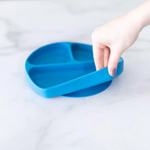 Load image into Gallery viewer, A hand holds a Bumkins Silicone Grip Dish: Dark Blue, demonstrating the suction cup bottom on a marble surface.