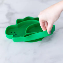 Load image into Gallery viewer, A hand holds a Bumkins Silicone Grip Dish, Special Edition: Dino, demonstrating the suction cup bottom on a marble surface.