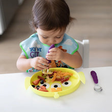 Load image into Gallery viewer, A toddler self-feeds from a Bumkins Silicone Grip Dish: Toy Story Alien with purple utensils at a white table.