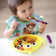Load image into Gallery viewer, A toddler self-feeds pasta and fruit from a Bumkins Silicone Grip Dish: Toy Story Alien, wearing a bib with cartoon characters.