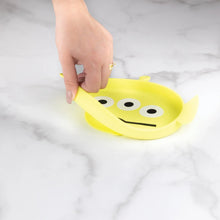 Load image into Gallery viewer, A hand holds a Bumkins Silicone Grip Dish: Toy Story Alien, demonstrating the suction cup bottom on a marble surface.