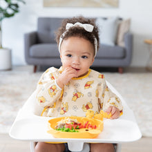 Load image into Gallery viewer, A toddler with a white headband in a high chair enjoys a meal from a Bumkins Silicone Grip Dish: Winnie The Pooh, wearing a yellow bib.