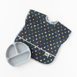 Bumkins Junior Bib: Super Mario™ Lineup lays flat on a white background next to a gray silicone divided plate.