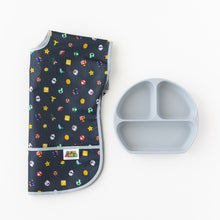 Load image into Gallery viewer, Bumkins Junior Bib: Super Mario™ Lineup lays folded on a white background beside a gray silicone divided plate.