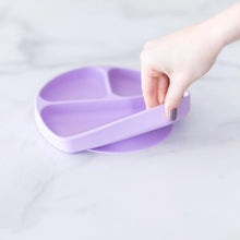 Load image into Gallery viewer, A hand holds a Bumkins Silicone Grip Dish: Lavender, demonstrating the suction cup bottom on a marble surface.