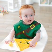 Load image into Gallery viewer, A curly-haired toddler in a high chair, wearing a green bib, eats from a Bumkins Silicone Grip Dish: Zelda™ Triforce on the tray.