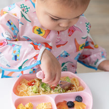 Load image into Gallery viewer, Close-up of a child in a pink patterned bib eating a meal from a Bumkins Silicone Grip Dish: Pink with a pink fork.