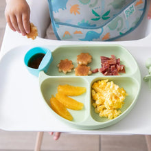 Load image into Gallery viewer, Close-up of a child in a high chair with a Bumkins Silicone Grip Dish: Sage filled with breakfast foods and a blue cup of syrup on the tray.