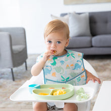 Load image into Gallery viewer, A boy with bright eyes eats breakfast in a high chair from a green plate, wearing a Bumkins SuperBib® 3 Pack: Hangry, Dinosaurs, Blue Tropic.