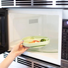 Load image into Gallery viewer, A person places a Bumkins Silicone Grip Dish: Sage with food into an open microwave.