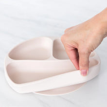 Load image into Gallery viewer, A hand holds a Bumkins Silicone Grip Dish: Sand, demonstrating the suction cup bottom on a marble surface.