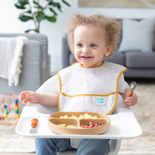 Load image into Gallery viewer, A smiling toddler in a high chair holds a spoon next to a Bumkins Silicone Grip Dish: Wood Grain filled with food.