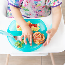 Load image into Gallery viewer, A child in a high chair wearing a colorful bib enjoys kiwi, eggs, tomatoes & a pastry from a Bumkins Silicone Grip Dish: Blue Jelly.