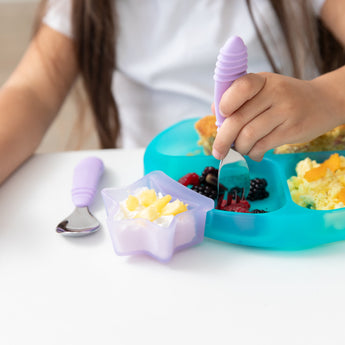 A child enjoys breakfast from a Bumkins Silicone Grip Dish: Blue Jelly, using a lavender fork, with yogurt and pineapple in a star bowl.