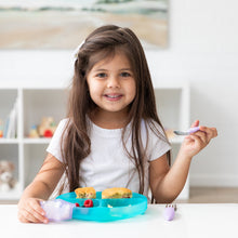 Load image into Gallery viewer, A young girl with long brown hair smiles while eating from a Bumkins Silicone Grip Dish: Blue Jelly at a white table.