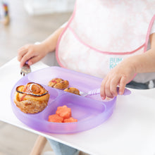 Load image into Gallery viewer, A child with a bib sits at a highchair, holding a fork and Bumkins Silicone Grip Dish: Purple Jelly with sweet rolls and fruit.