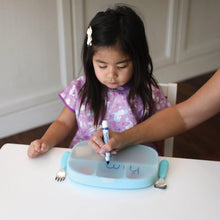 Load image into Gallery viewer, An adult hand writes on the lid of Bumkins Silicone Grip Dish with Lid (5 Section): Blue at a white table while a child sits nearby.