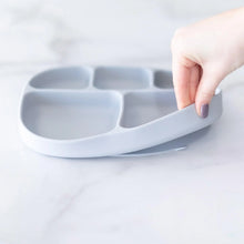 Load image into Gallery viewer, A hand holds a Bumkins Silicone Grip Dish with Lid (5 Section): Gray, demonstrating the suction cup bottom on a marble surface.