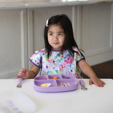 Load image into Gallery viewer, A young girl in a colorful bib sits at a white table with a Bumkins Silicone Grip Dish with Lid (5 Section): Lavender and matching utensils.