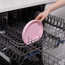 Load image into Gallery viewer, A hand places a Bumkins Silicone Grip Plate: Pink into the top rack of an open dishwasher.