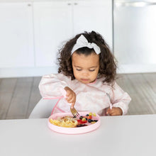Load image into Gallery viewer, A toddler enjoys scrambled eggs and berries from a Bumkins Silicone Grip Plate: Pink while sitting in a white kitchen.