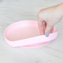 Load image into Gallery viewer, A hand holds a Bumkins Silicone Grip Plate: Pink, demonstrating the suction cup bottom on a marble surface.