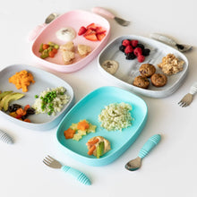 Load image into Gallery viewer, Four colorful plates, including Bumkins Silicone Grip Tray: Blue, with assorted healthy foods for kids and utensils on a white background.