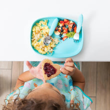 Load image into Gallery viewer, Top-down view of a child eating toast with jam while a Bumkins Silicone Grip Tray: Blue with scrambled eggs and fruit sits on a white table.