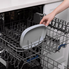 Load image into Gallery viewer, A hand places a Bumkins Silicone Grip Tray: Gray into the top rack of an open dishwasher.