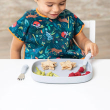 Load image into Gallery viewer, A child in a bib sits at a table, eating star sandwiches, green snacks, and raspberries from Bumkins Silicone Grip Tray: Gray using cutlery.