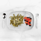 Bumkins Silicone Grip Tray: Marble holds spinach pasta, cherry tomatoes, and olives with matching utensils nearby on a marble background.