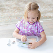 Load image into Gallery viewer, A young blonde child in a purple bib sits at a white table, removing a lid from a Bumkins Silicone Grip Tray: Marble.