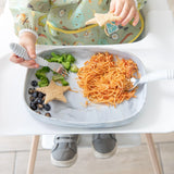 A child in a high chair enjoys pasta, broccoli, and blueberries from a Bumkins Silicone Grip Tray: Marble with a fork.