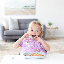 Load image into Gallery viewer, A little blonde girl in a purple bib happily eats from a Bumkins Silicone Grip Tray: Marble with a spoon at a white table.